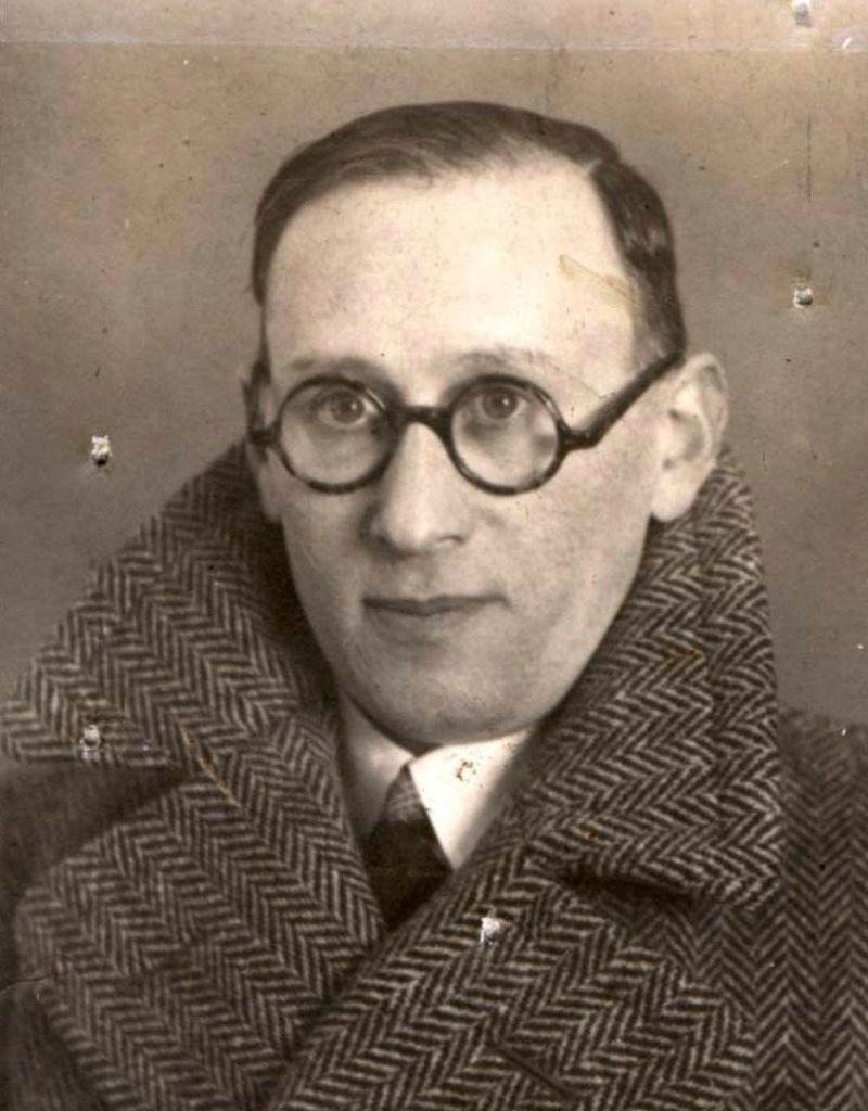 A vintage black and white portrait of a man wearing round glasses and a herringbone coat.