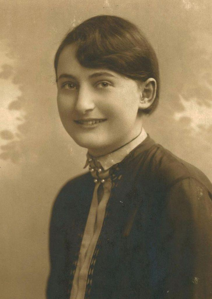 Vintage sepia-toned portrait of a smiling woman in a dark blouse with a high collar and a patterned tie.
