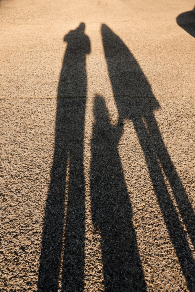 Photo of the shadows of my wife, our daughter and me. I'm standing on the left side, slightly leaning to the middle, where my little daughter stands, while holding hands with her mother, to the right