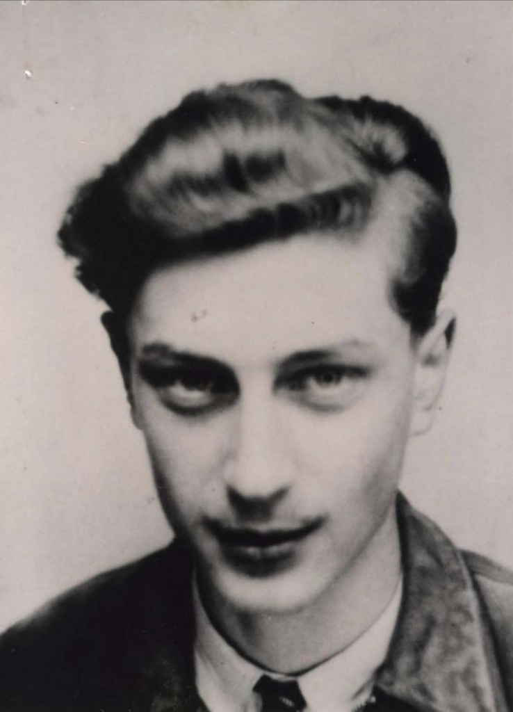 Black and white portrait of a young man with slicked-back hair, wearing a dark jacket and tie.