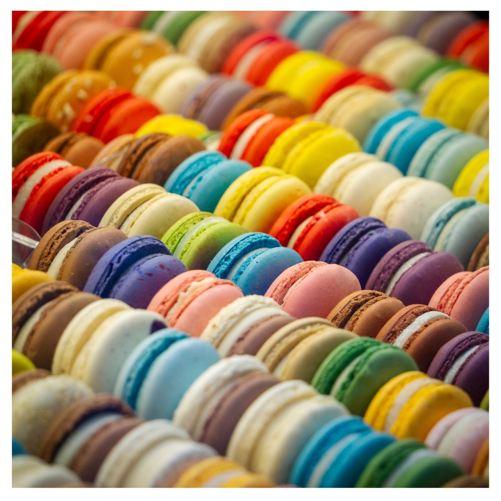 Ein kleines Rudel Macarons in allen Farben des Regenbogens fein säuberlich in der Auslage einer Bäckerei drappiert. 