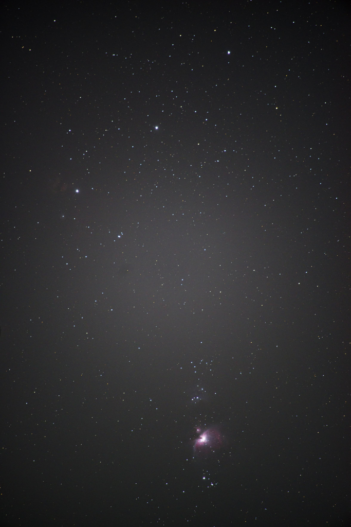 A starry sky with three bright stars in a diagonal across the top. Near the bottom of the frame, a faint pink and purple nebula glows between clusters of stars.