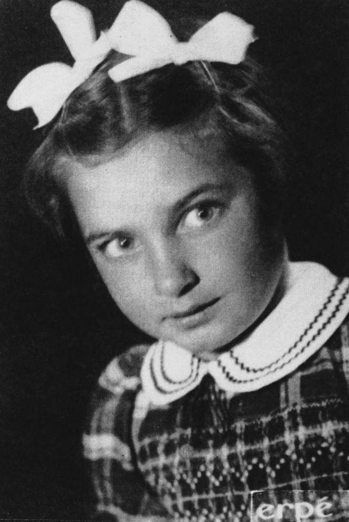 Black and white portrait of a young girl wearing a bow in her hair and a patterned dress, looking contemplatively to the side.
