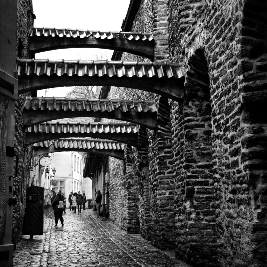 view of an old narrow street in the old town of Tallinn. Stone walls with arches across the street. black and white photo, square format