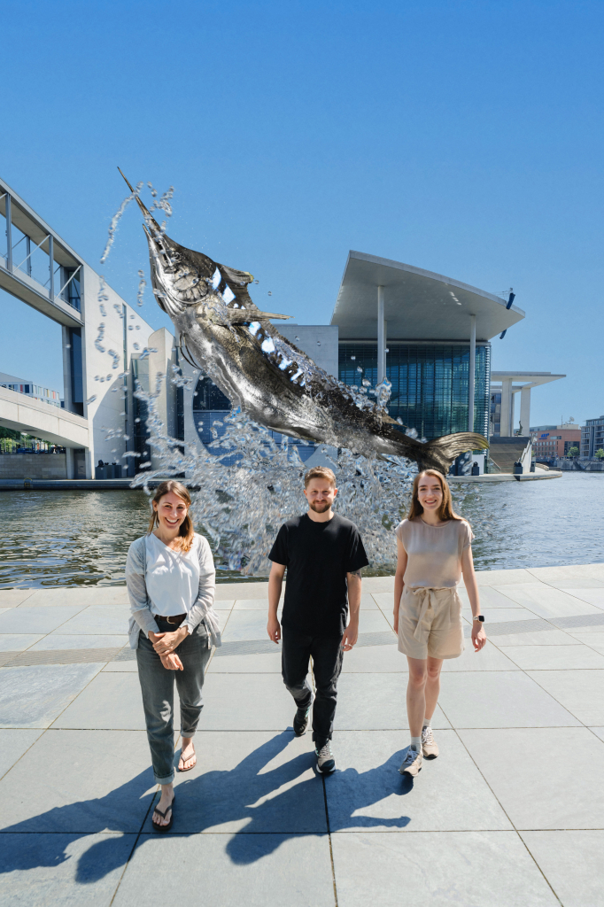 v.l.n.r.: die Forschenden Dr. Alicia Burns, David Mezey und Dr. Palina Bartashevich, im Hintergrund springt ein gestreifter Marlin aus der Spree. Foto: Berlin University Alliance