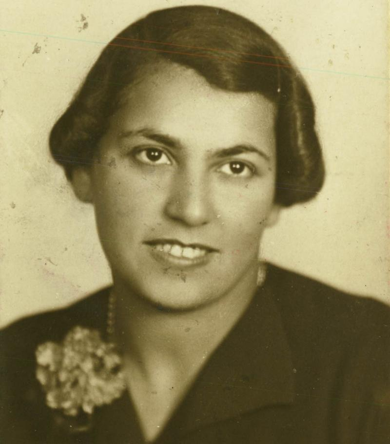 Vintage portrait of a woman, featuring a close-up of the individual smiling, wearing a dark jacket with a floral brooch.