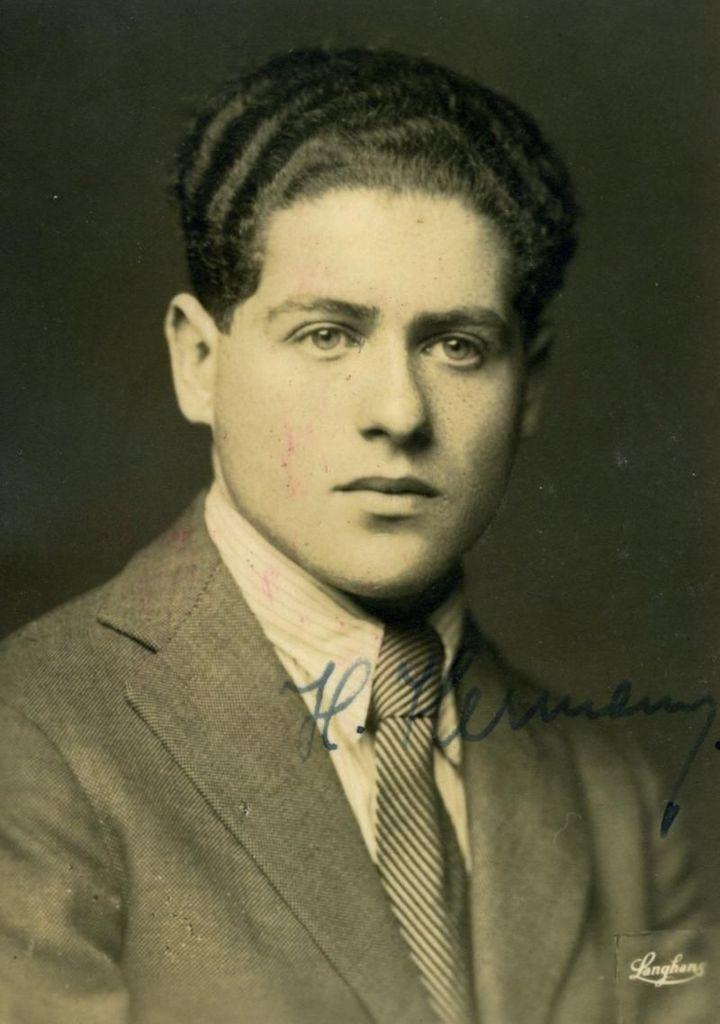 Vintage black and white portrait of a man with curly hair, wearing a suit and tie. The photo includes an autograph.