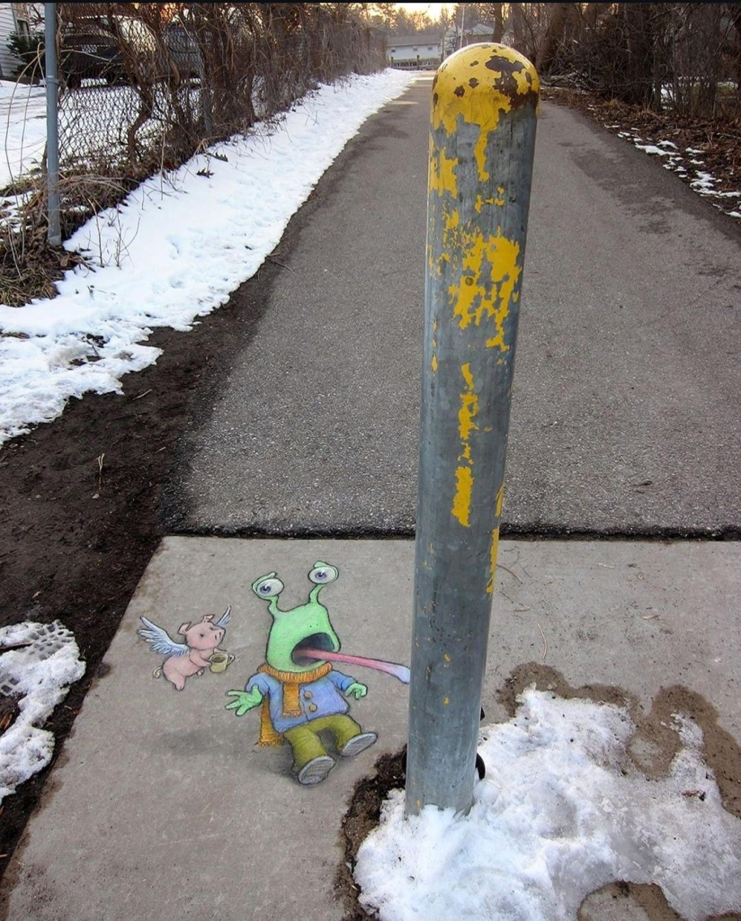 Streetart. A green snail and a flying pig were drawn with chalk on a gray sidewalk right next to an iron bollard. The snail (called Sluggo) is neon green, has stalk eyes and wears winter clothing. It has stuck out its long tongue and is now stuck to the iron bollard. A little flying pig (namens Philomena) rushes over with a hot cup of tea to help the horrified Sluggo. 
Info: A Repost by David Zinn in January 2025 with the note "Be careful out there!". (It's too cold in Ann Arbor to draw with chalk at the moment).