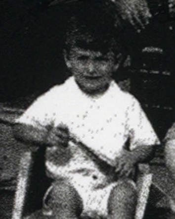 A vintage black and white photo of a young boy sitting, holding a stick.