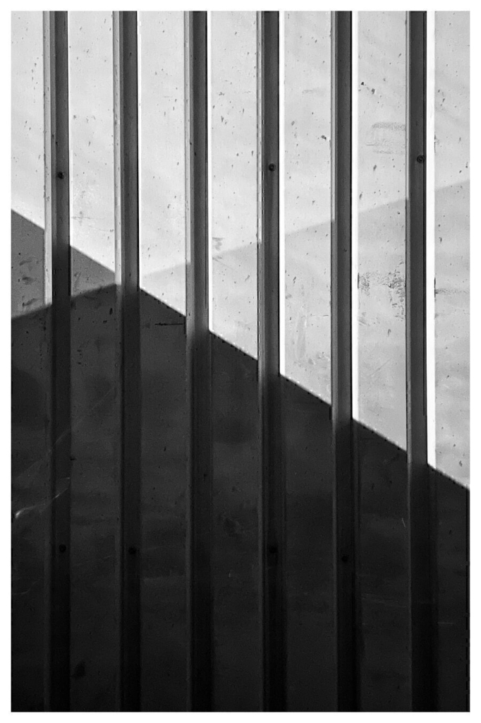 Abstract black and white composition featuring vertical lines and geometric shapes created by contrasting light and shadow on a textured surface.