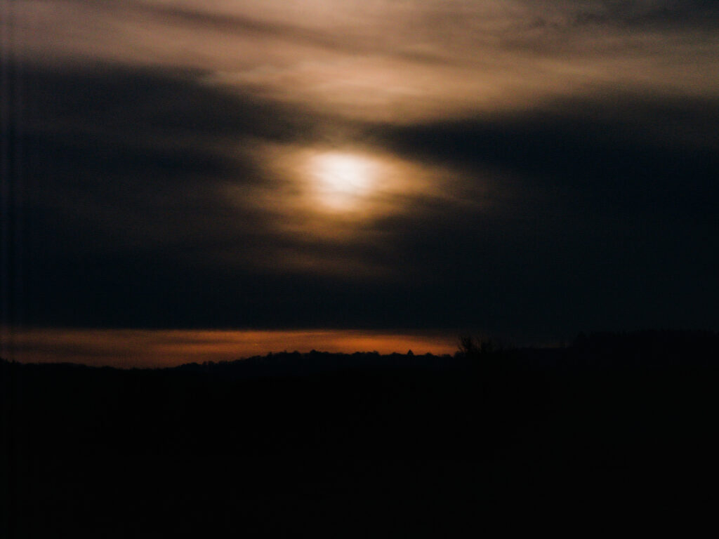 The sun hidden behind dark clouds, dark hills in the foreground