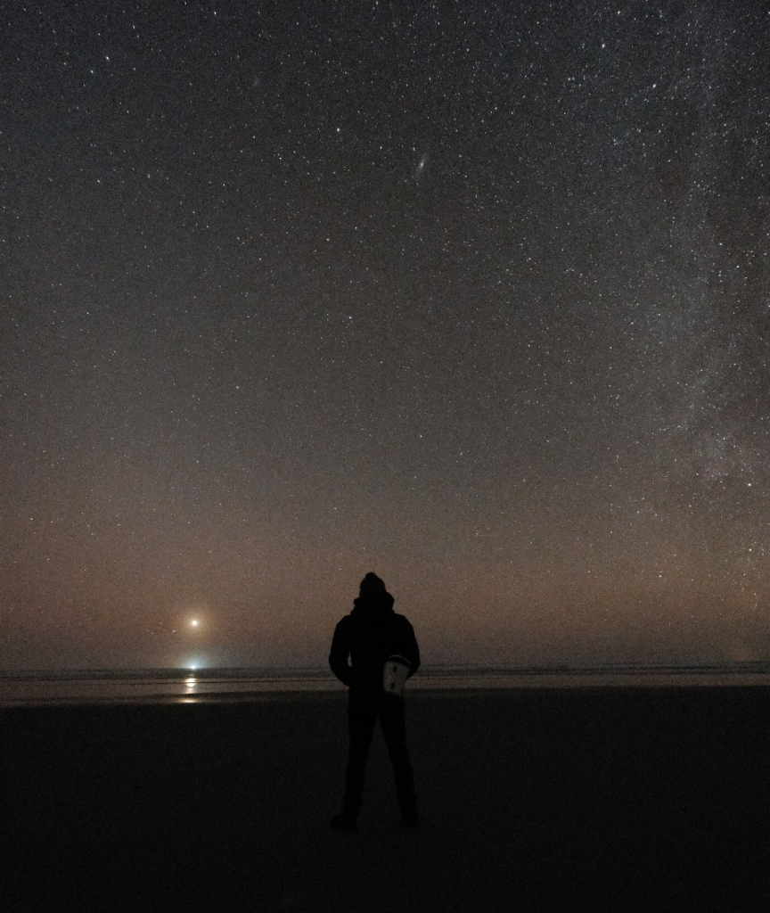 Picture of night sky, person standing up on the beach with Venus and the Milky Way visible.