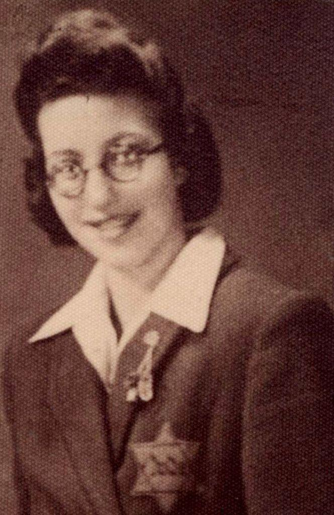 Vintage sepia-toned portrait of a woman wearing glasses, a dark jacket, and a lapel pin. A Jewish start with the word "Jude" is visible on her jacket.