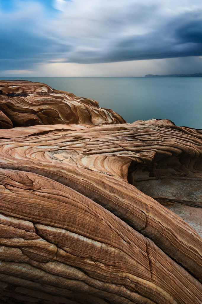 sandstone formation looking like waves with stormy ocean in the back