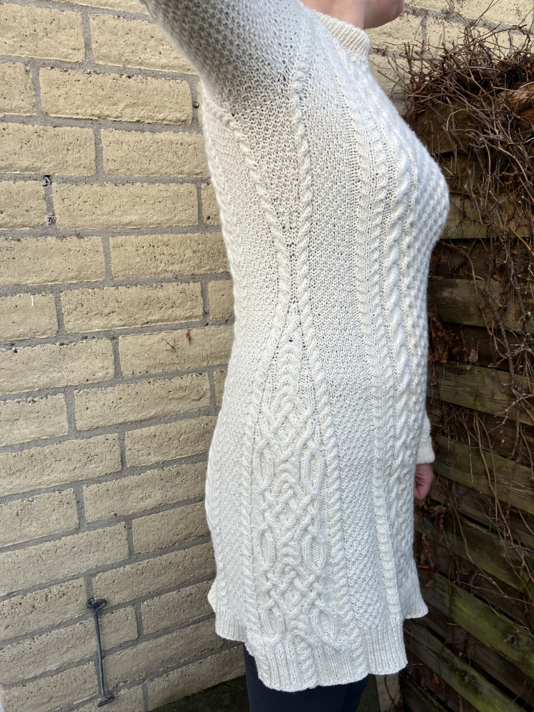 Side view showing waist shaping going inwards over moss stitch and outwards into a symmetrical “Celtic” cable