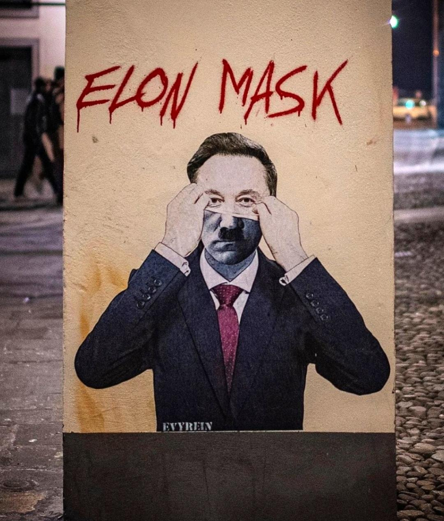 Streetartwall. A mural depicting Elon Musk was sprayed onto a narrow gray concrete wall using stencils. Above the image, "Elon MASK" is written in red lettering and below it, the man in the black suit can be seen pulling a mask off his face. The upper half of his face is Elon Musk, the lower half looks like Adolf Hitler. These kinds of satirical works of art in public spaces in Italy don't usually survive for long. So you should be quick to photograph it.
Info: Evyrein" is a well-known Italian street artist whose art often thrives on contrasts. The seemingly familiar is placed in a new, mostly satirical context. He says: "I want to calm the waves, make people think, shake up their conscience. I want people to pause, if only for a moment, and ask themselves what is happening in the world around them.