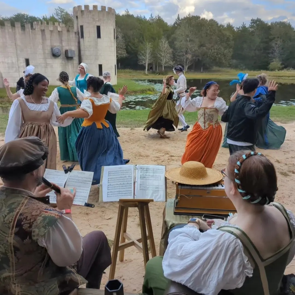 Members of the Moonlight Renaissance Dance troupe dancing in front of a castle (a modern recreation of one) to live music performed by renaissance reenactment musicians.

Whitney Rowlett manages the troupe and offers both performances and dance lessons.