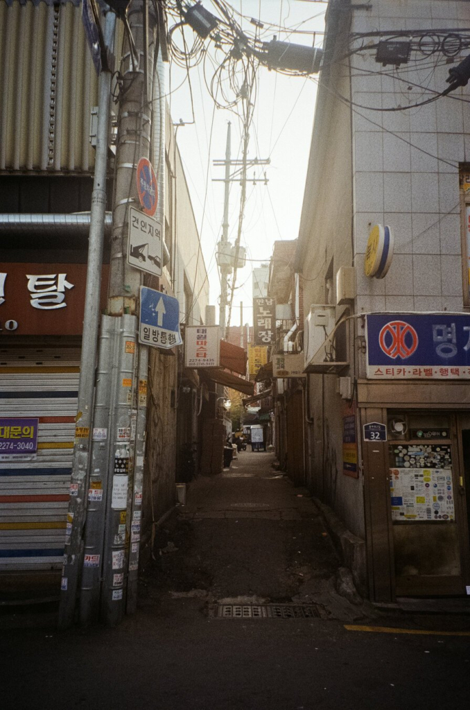 건물 사이 사람 서너 명이 지나갈 수 있을 법한 좁은 골목. 입구쪽 전봇대에 '일방통행'이란 표지가 보인다.