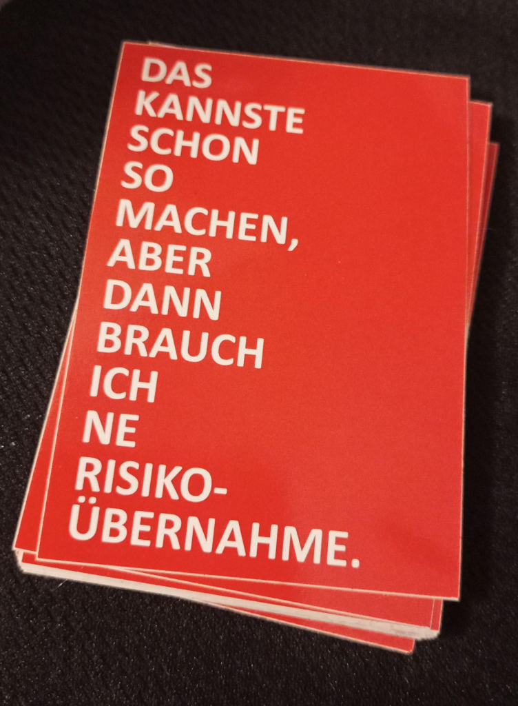 Ein Stapel roter Sticker mit dem weissen Text "DAS KANNSTE SCHON SO MACHEN, ABER DANN BRAUCH ICH NE RISIKO-ÜBERNAHME."