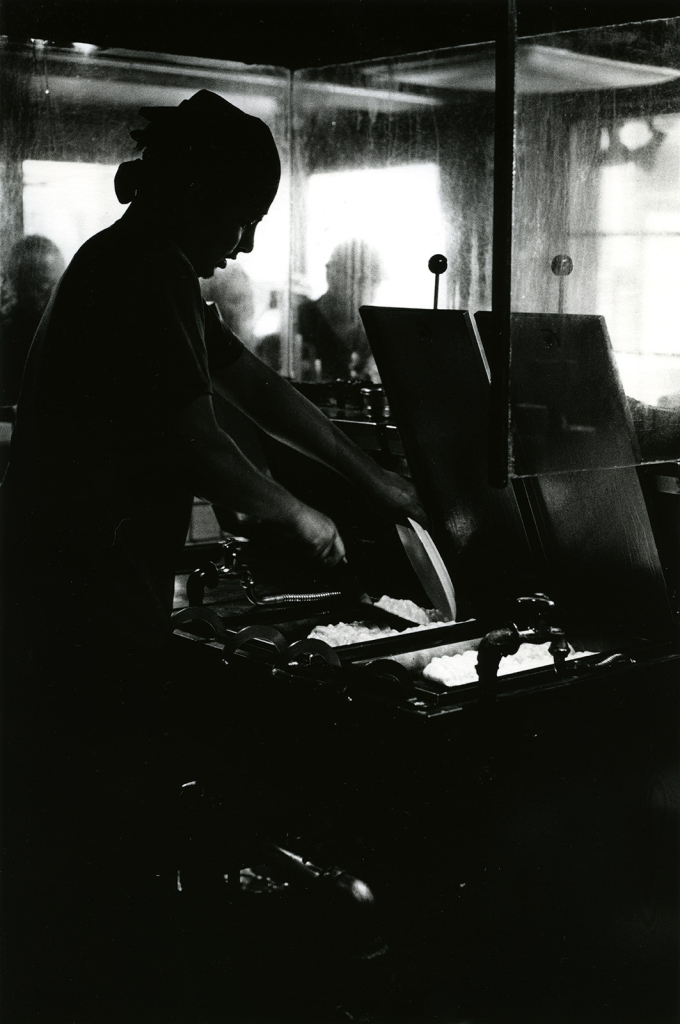 Photo en noir et blanc prise à contre-jour d'un cuisinier qui prépare des gyozas dans un restaurant typique de Tokyo.