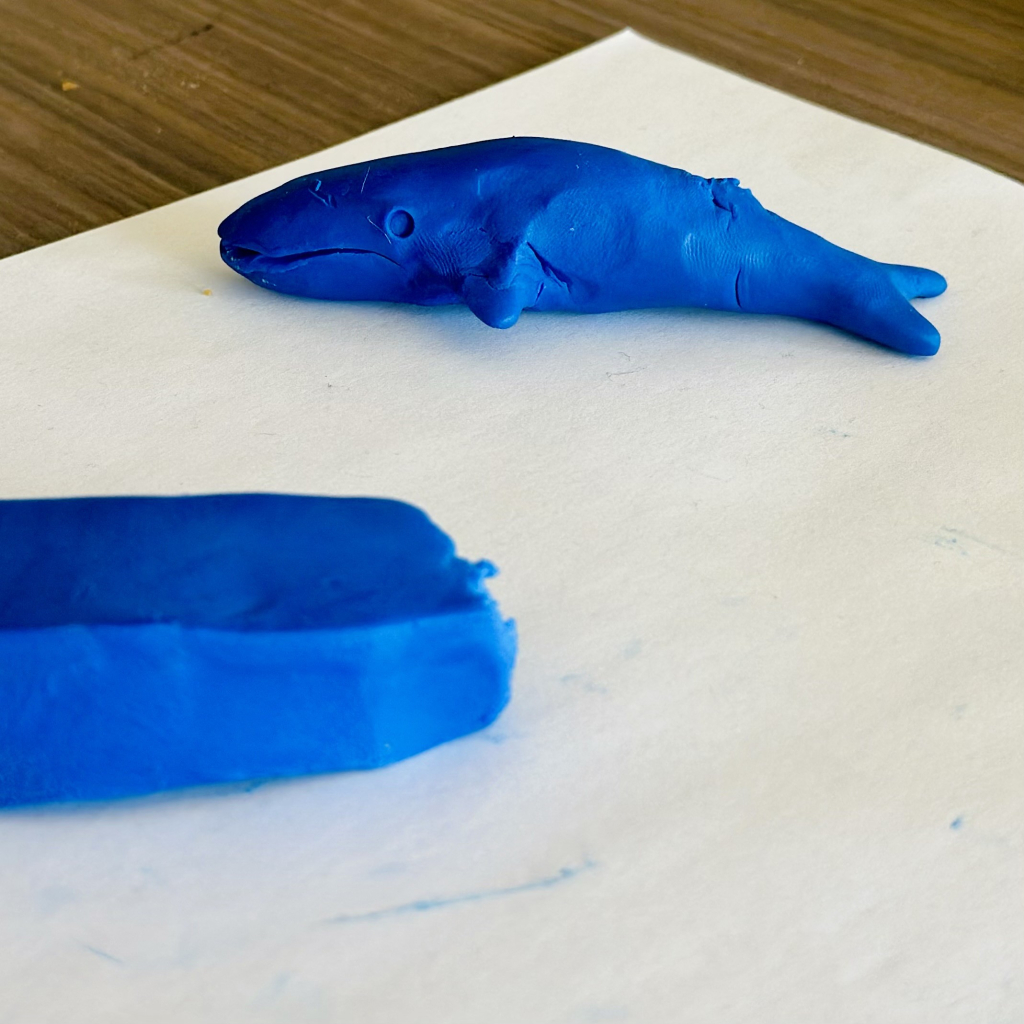 A photo of some playdoh like clay that is blue. One of it is a big block that is not molded and the other piece is a whale that looks pretty convincing 