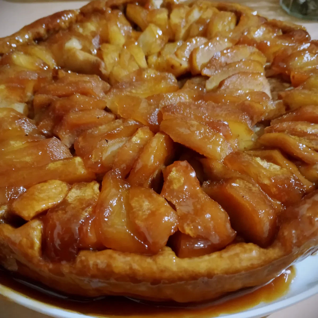 Photo en gros plan d'une tarte tatin avec le caramel qui a bien imbibé les pommes et qu'on voit également sur le plat.