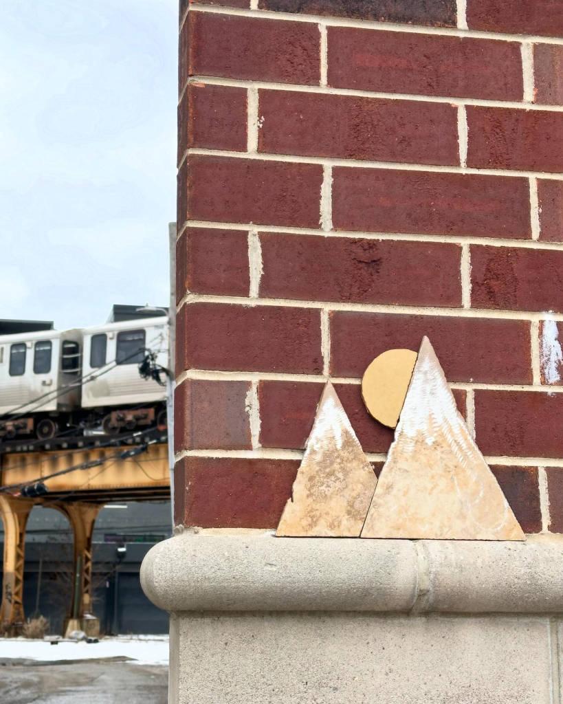 Street art of two woodcut triangular mountains with a sun setting behind one. In the background, the subway is visible on the elevated tracks. 