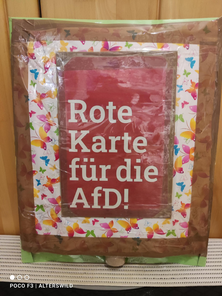 Rückseite:
Schmetterlings-Geschenkpapier als Untergrund, darauf eine Pappe, roter Untergrund, weiße Schrift 
"Rote
Karte
für die 
AFD!