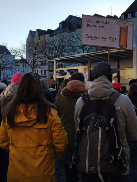 Bilck aus der 10. Reihe auf die Bühne der Abschlusskundgebung: 

Demoschild mit Kölschstange, wo ein Deckel drauf liegt. 

Tex: Da drinkste keine met. Sag nein zur AfD.