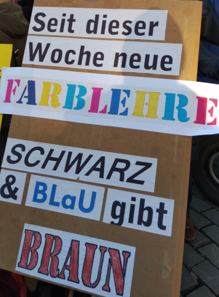 Demoschild mit der Aufschrift Seit dieser WOche neue Farbenlehre: Schwarz und BLaU gibt BRAUN