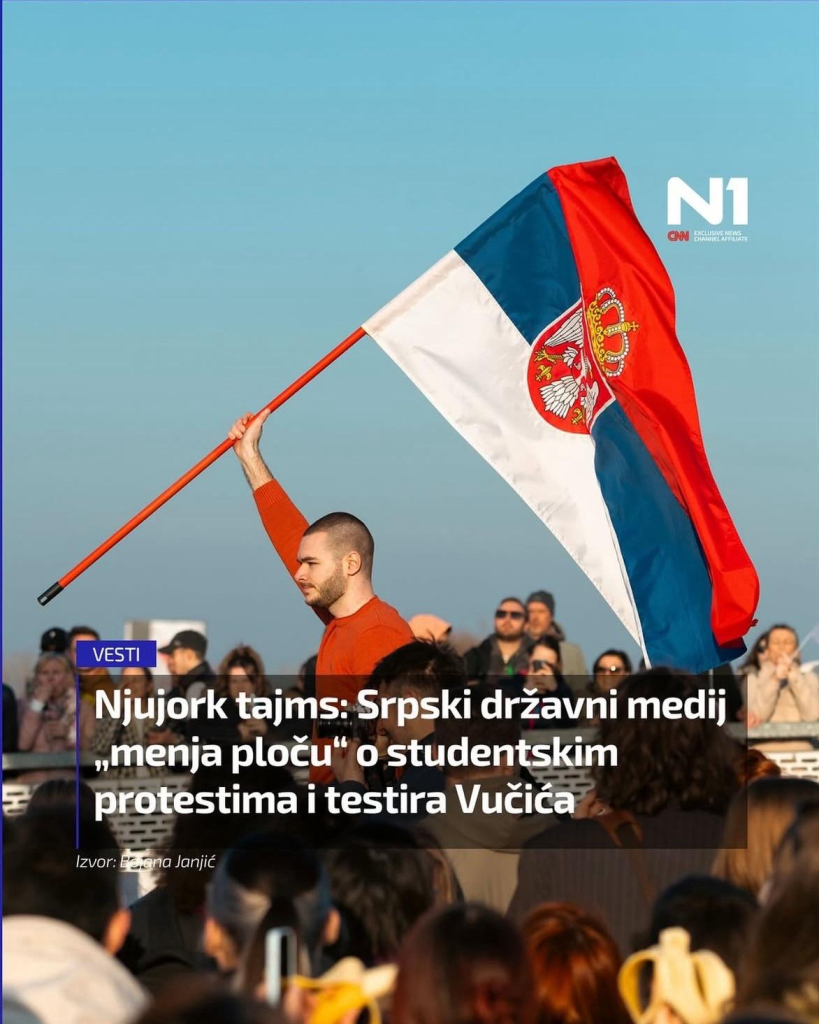 Sharepic zeigt einen jungen Mann mit kurz geschorenem Haar und einem roten Pullover, der eine große serbische Flagge mit einem orangefarbenen Fahnenmast schwenkt. Er steht vor einer Menschenmenge, die größtenteils aus jungen Erwachsenen besteht. Viele in der Menge schauen in seine Richtung, einige tragen Sonnenbrillen. Der Himmel ist klar und blau, was darauf hindeutet, dass es ein sonniger Tag ist. Das Bild hat einen Nachrichtentitel von N1, einer serbischen Nachrichtenplattform, der sich auf die Berichterstattung staatlicher Medien über Studentenproteste und den serbischen Präsidenten Aleksandar Vučić bezieht: „New York Times: Serbische Staatsmedien „wechseln den Kurs“ bei den Studentenprotesten und testen Vučić.“