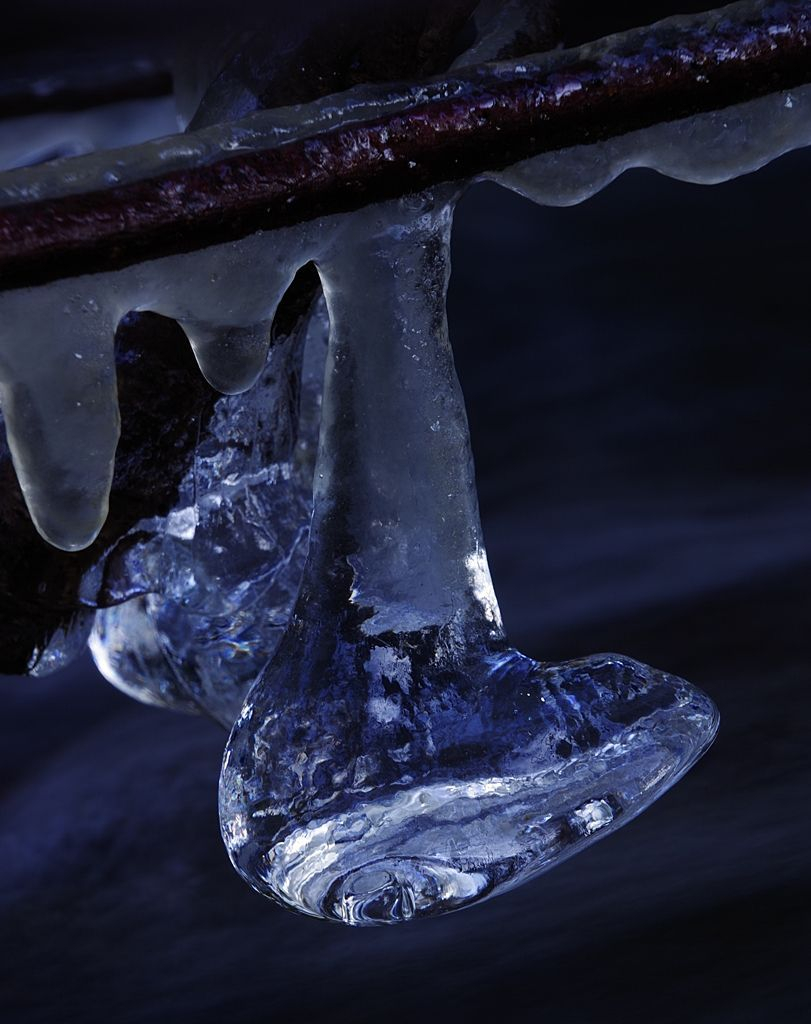 Two icicles haning on a branch over a brook. One of them is in front of the other and they look like a pair of boots. Some light is shining throuh them and make them look like they where made of glass.