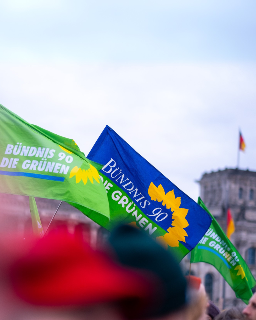 Foto von einer Demonstration vor dem Reichstagsgebäude, in der Bildmitte drei Fahnen der Partei BÜNDNIS 90/DIE GRÜNEN.