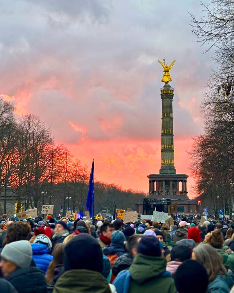 Foto des Demonstrationszuges vor der Siegessäule in Berlin, im Hintergrund Wolken im Abendrot.