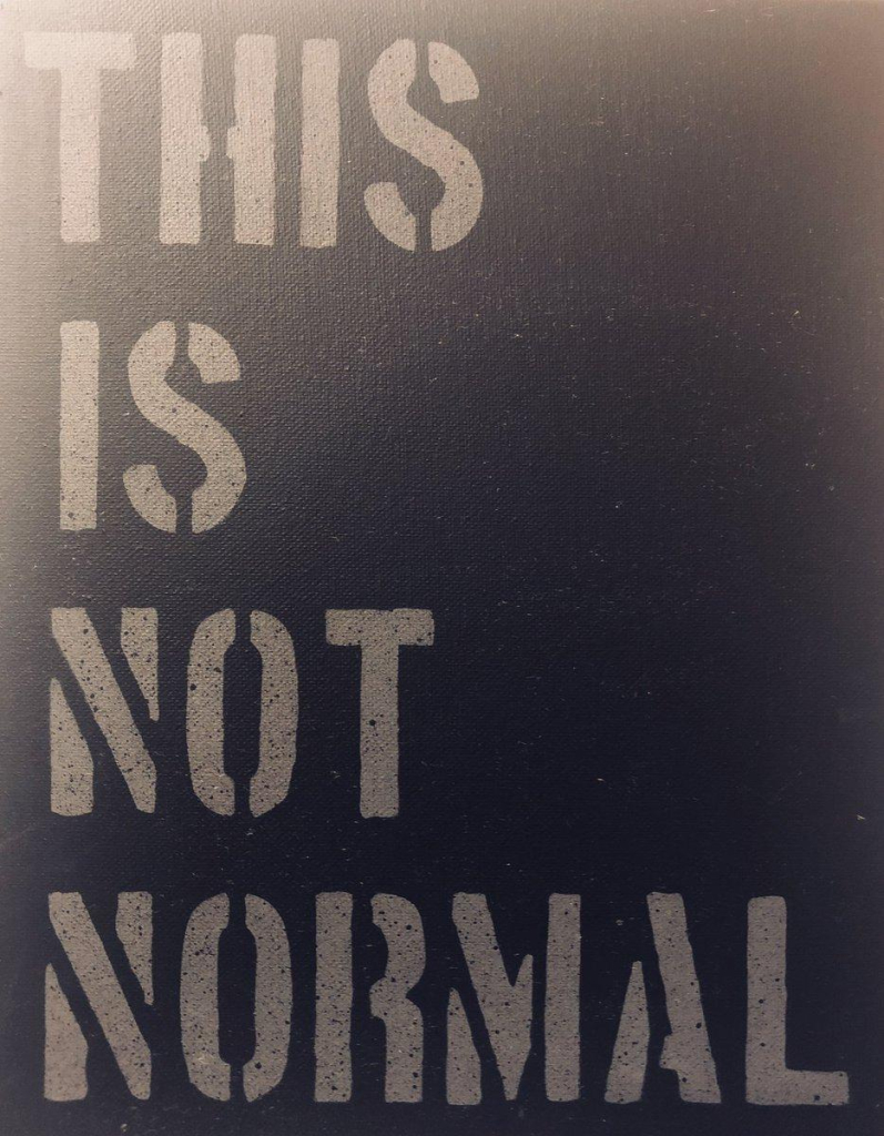 Stencil art. Grey lettering on dark background, all caps: "THIS IS NOT NORMAL"