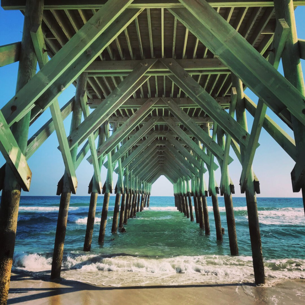 The view from the beach under a pier looking toward the water.