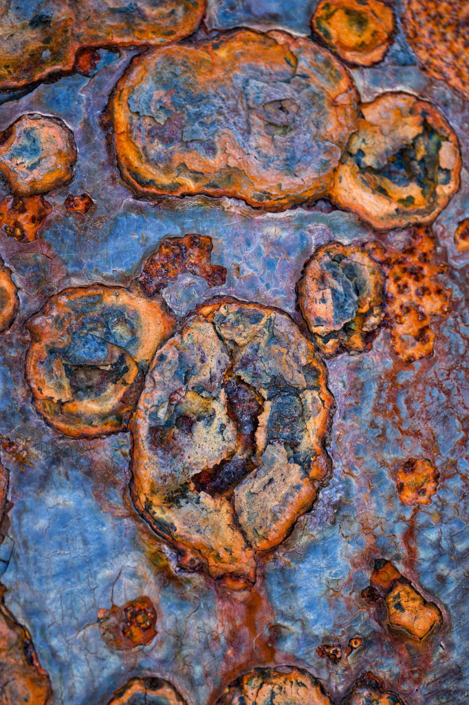 Close-up image showing the incredible textures and colours created by salty sea air on the pock-marked surface of coastal ironworks, with blues, purples, greens and browns making the iron look like the surface of a distant planet or meteorite