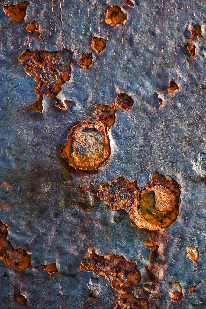 Close-up image showing the incredible textures and colours created by salty sea air on the pock-marked surface of coastal ironworks, with blues, purples, greens and browns making the iron look like the surface of a distant planet or meteorite