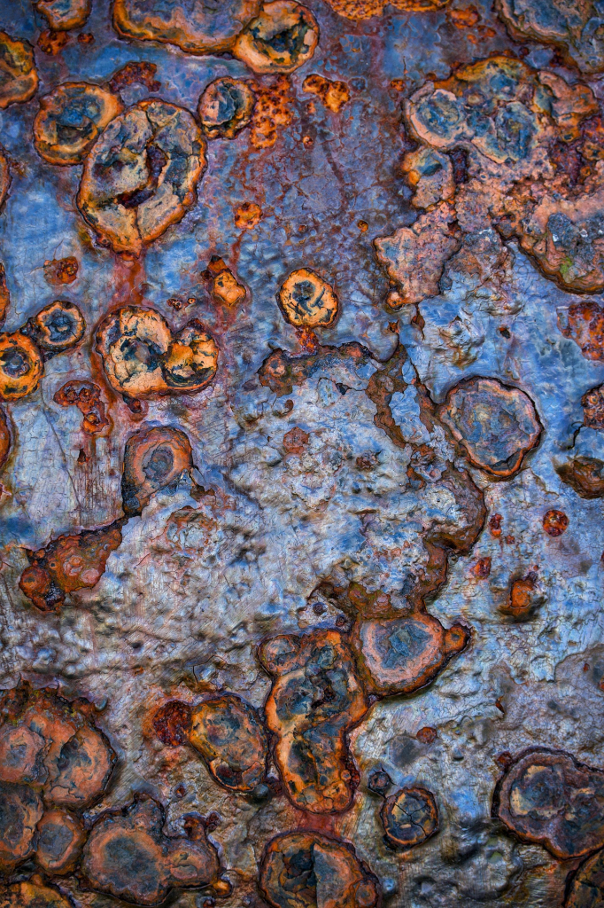 Close-up image showing the incredible textures and colours created by salty sea air on the pock-marked surface of coastal ironworks, with blues, purples, greens and browns making the iron look like the surface of a distant planet or meteorite