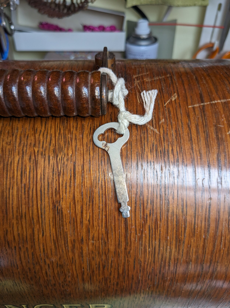 Close up of a laughably simple metal key tied with string to the handle of the bentwood case.