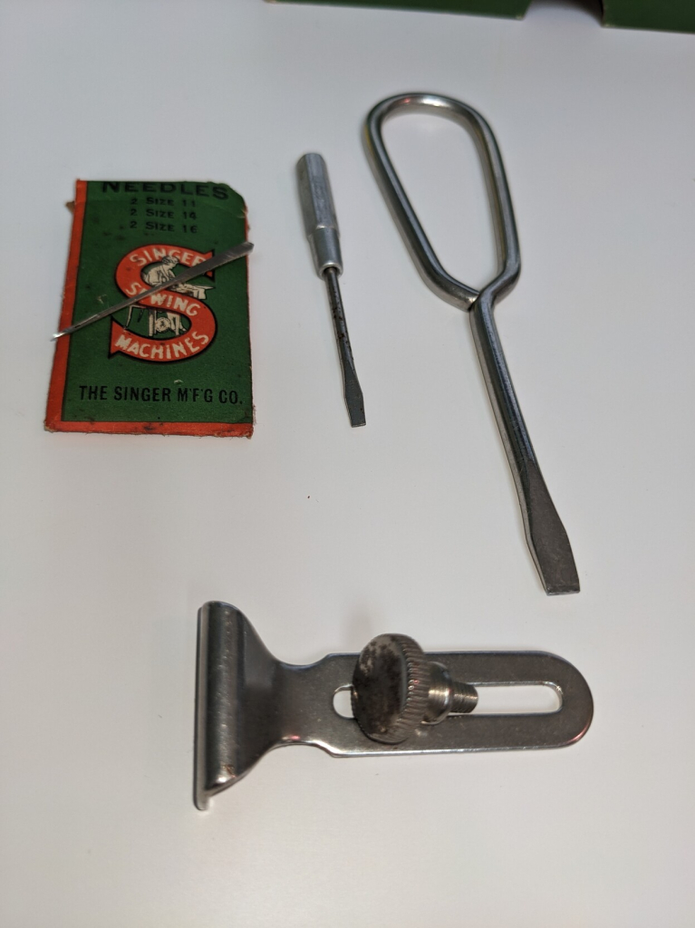 A packet of needles two screwdrivers and Singer "SIMANCO" part number 26627, which is an adjustable seam allowance marker