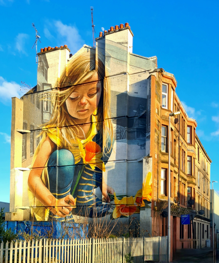 A mural on an expiaed gable of a Glasgow tenement of a young girl picking daffodils .