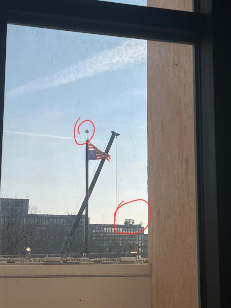 Looking out a window at a flag pole with an upside down American flag 