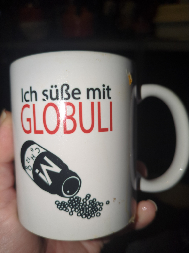 Kaffetasse mit der Aufschrift "ich süße mit GLOBULI" und der Abbildung eines offenen Arznei Fläschchens, aus dem die Zuckerperlen kullern Merch von Methodisch inkorrekt