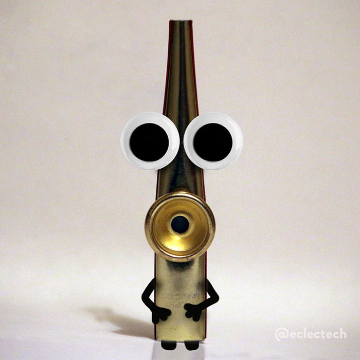 A square photo of a shiny gold kazoo standing on end against a white backdrop.  The round funnel on the top is facing the camera, and has been repurposed as a surprised mouth. Above are two large googly eyes, and there are arms and feet drawn on below. It is definitely saying "oooooh!"