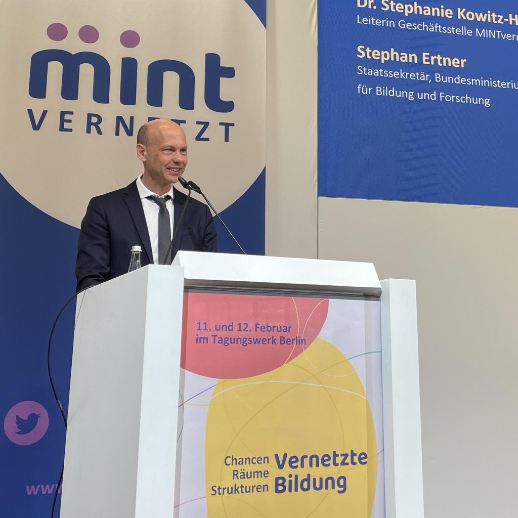 Stephan Ertner, Staatsekretär im Bundesministerium für Bildung und Forschung, steht am Rednerpult von "mintvernetzt". Im Hintergrund das Banner mit dem Logo der Veranstaltung. An der Vorderseite des Pults der Schriftzug "11. und 12. Februar im Tagungswerk Berlin. Chancen, Räume, Strukturen, Vernetzte Bildung".