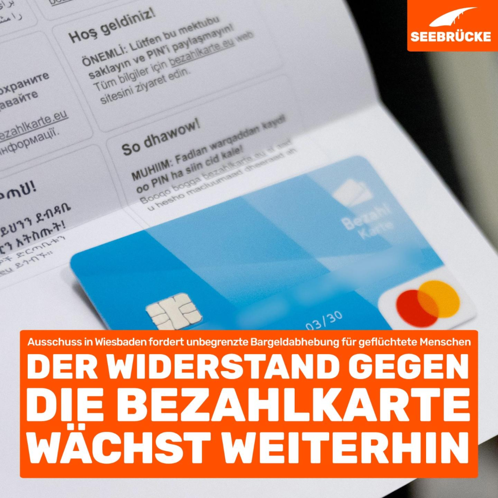 Foto einer Bezahlkarte vor einem Infozettel. In einem orangen Kasten steht “Ausschuss in Wiesbaden fordert unbegrenzte Bargeldabhebung für geflüchtete Menschen. Der Widerstand gegen die Bezahlkarte wächst weiterhin.”. In der rechten oberen Ecke ist das Seebrücke-Logo in weiß auf orange.