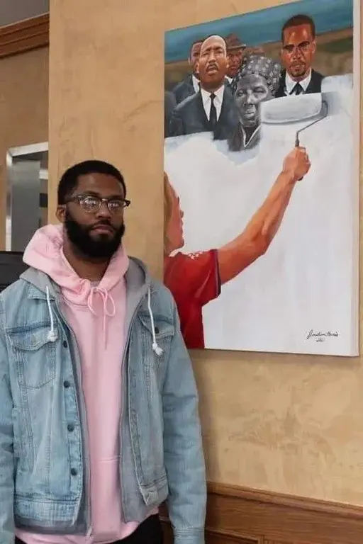 Jonathan Harris standing before his painting depicting a white person using a paint roller to white wash over the faces of luminaries of Black American history (Harriet Tubman, Malcolm X, Martin Luther King Jr., etc)