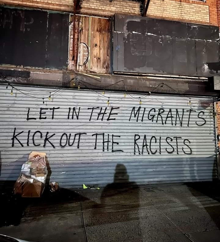 "Let in the migrants, kick out the racists" written on a roller door with black spray paint