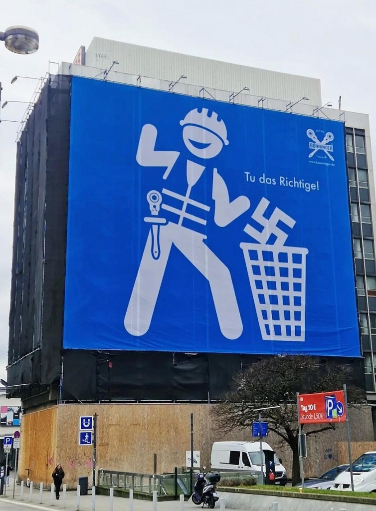 Streetart. A blue banner measuring around 500 square meters hangs on the outside wall of Dortmund Central Station, proclaiming a clear message against right-wing extremism. The poster shows a huge pictogram with a stylized craftsman. He is throwing a swastika into a garbage can. "Do the right thing" is written above it in German.
Info: "Right-wing extremist ideas belong in the garbage can, it's easier and nicer to live without them," reads the press release from the family business "Gerüstbau Bönninger. "...
We believe that you should officially stand up for your point of view. That's why we also use our scaffolding as a basis to get important messages out into the world in a striking way..